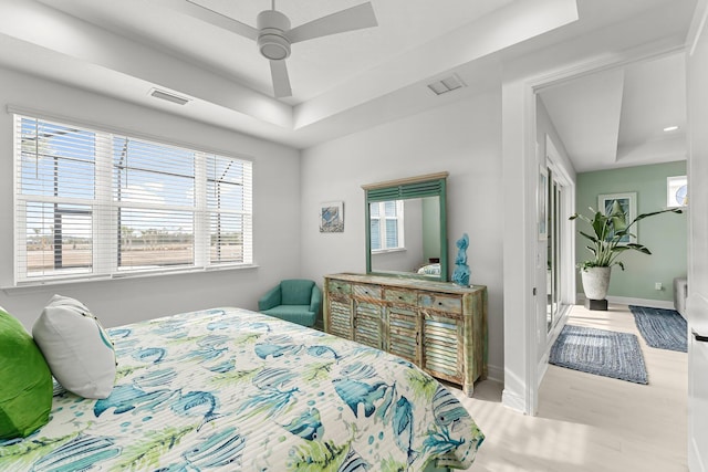 bedroom featuring a raised ceiling, light wood-type flooring, and ceiling fan