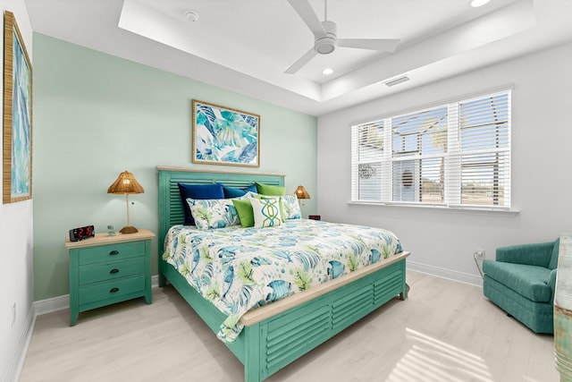 bedroom featuring light hardwood / wood-style floors, a raised ceiling, and ceiling fan