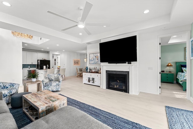 living room featuring ceiling fan, a raised ceiling, and light hardwood / wood-style flooring