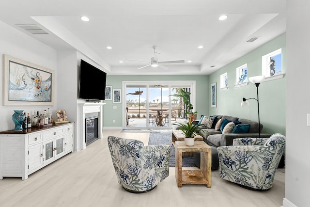 living room featuring ceiling fan, a raised ceiling, and light hardwood / wood-style floors