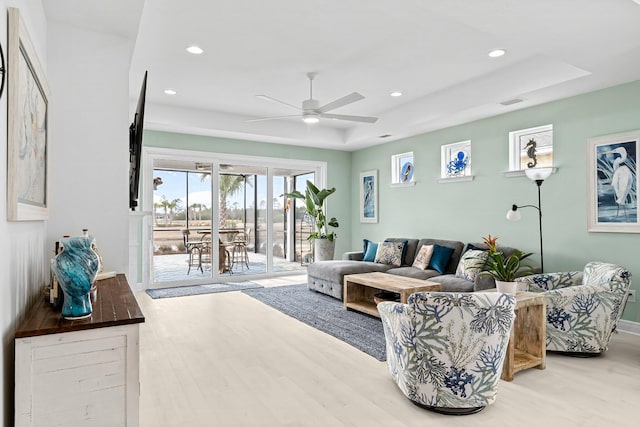 living room featuring a tray ceiling, light hardwood / wood-style floors, and ceiling fan