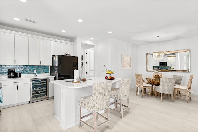 kitchen with wine cooler, white cabinetry, black fridge, pendant lighting, and backsplash