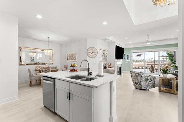 kitchen featuring sink, gray cabinetry, an island with sink, decorative light fixtures, and stainless steel dishwasher