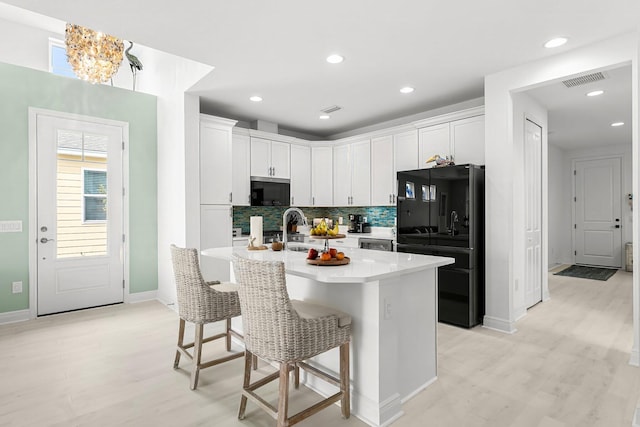 kitchen with black refrigerator, a kitchen breakfast bar, tasteful backsplash, and white cabinets