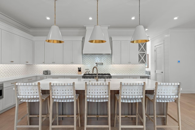 kitchen featuring decorative light fixtures, light hardwood / wood-style floors, an island with sink, and a kitchen bar