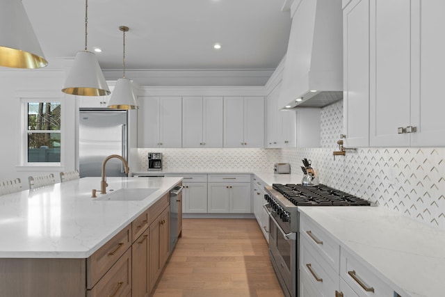 kitchen with sink, white cabinetry, high end appliances, light stone countertops, and custom range hood