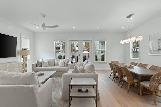 living room featuring crown molding, a wealth of natural light, ceiling fan with notable chandelier, and light wood-type flooring