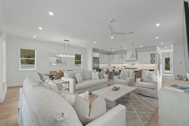 living room with ornamental molding, ceiling fan with notable chandelier, and light hardwood / wood-style floors