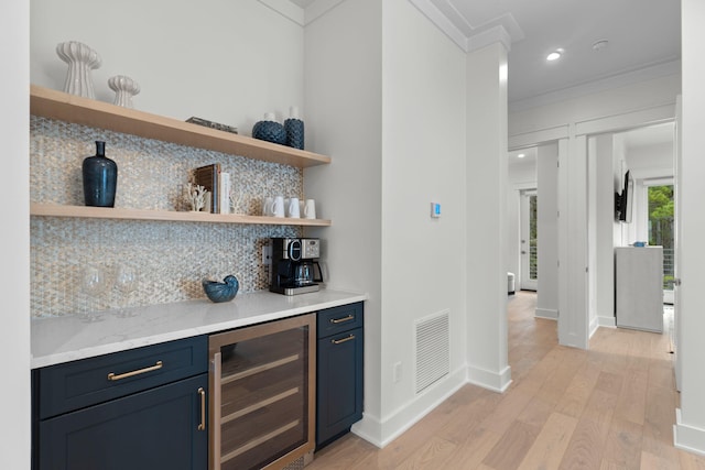 bar with tasteful backsplash, blue cabinets, beverage cooler, ornamental molding, and light hardwood / wood-style floors