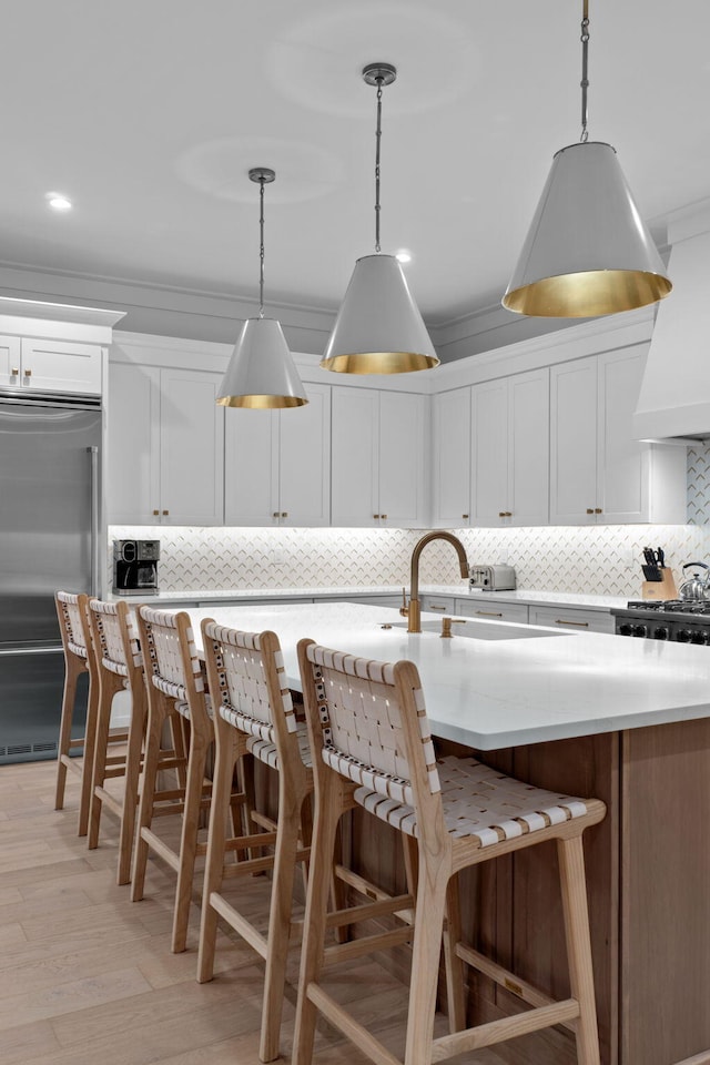 kitchen featuring high quality fridge, hanging light fixtures, a center island with sink, and white cabinets