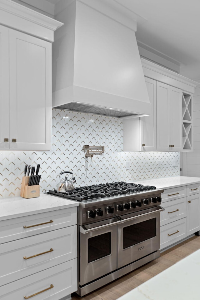 kitchen with white cabinetry, decorative backsplash, custom range hood, and range with two ovens