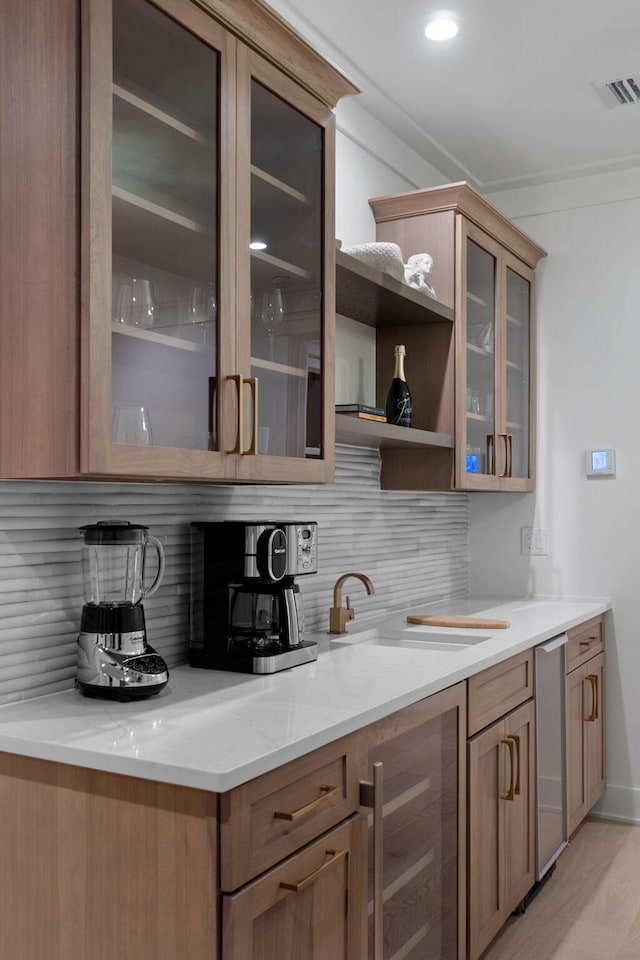 bar with wine cooler, sink, light stone countertops, light hardwood / wood-style floors, and decorative backsplash