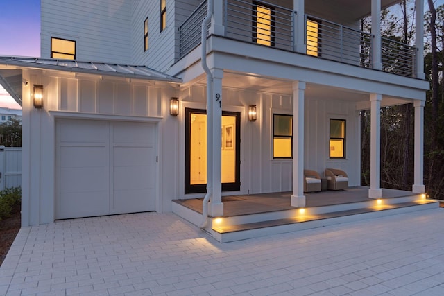 91 Pelayo Ave, Santa Rosa Beach, FL 32459 - exterior entry at dusk with board and batten siding, a balcony, a garage, a standing seam roof, and metal roof