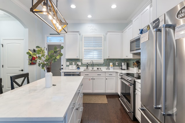 kitchen featuring high quality appliances, sink, white cabinets, and decorative light fixtures