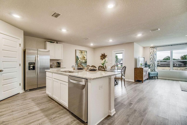 kitchen with appliances with stainless steel finishes, white cabinetry, sink, a center island with sink, and a textured ceiling