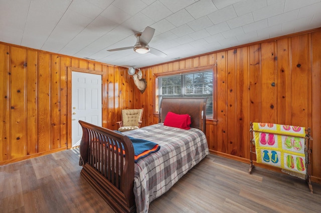 bedroom with hardwood / wood-style flooring, ceiling fan, and wood walls