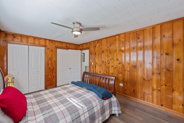 bedroom featuring multiple closets, hardwood / wood-style flooring, ceiling fan, and wood walls