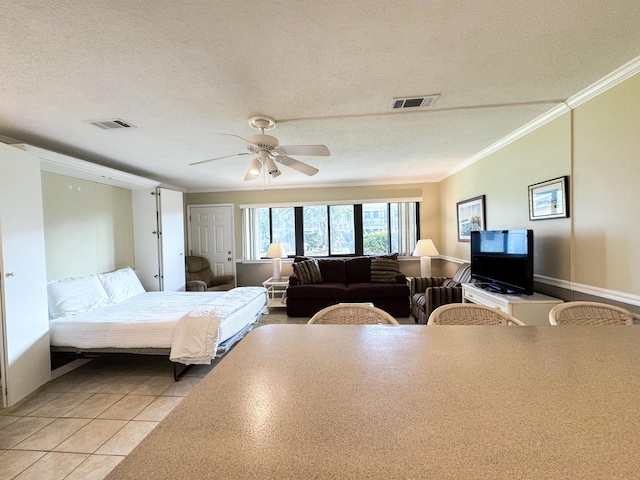 bedroom with ornamental molding, light tile patterned floors, ceiling fan, and a textured ceiling