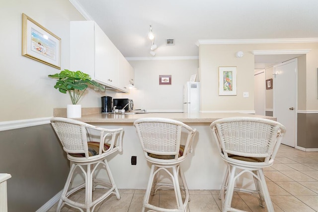 kitchen featuring a breakfast bar area, white cabinets, white refrigerator, ornamental molding, and kitchen peninsula