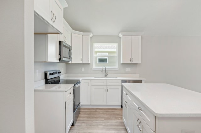 kitchen with light countertops, light wood-style floors, white cabinets, stainless steel appliances, and a sink