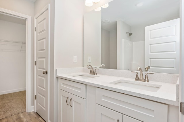 bathroom with a sink, baseboards, walk in shower, and double vanity