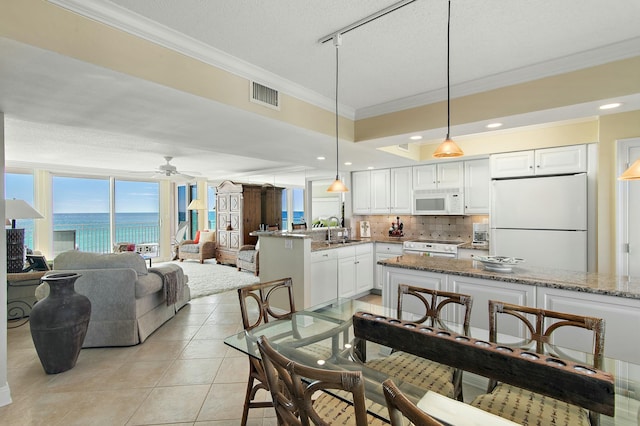 tiled dining area featuring sink, a water view, a textured ceiling, ornamental molding, and ceiling fan