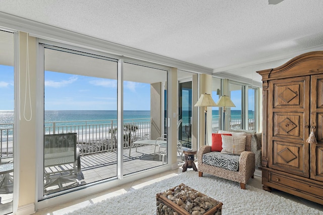 interior space featuring a view of the beach, crown molding, floor to ceiling windows, a water view, and a textured ceiling