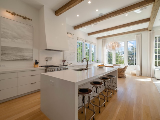 kitchen featuring sink, hanging light fixtures, an island with sink, white cabinets, and light wood-type flooring