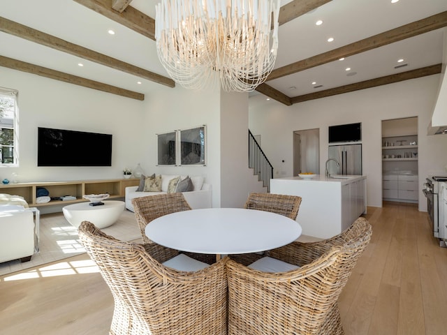 dining space featuring an inviting chandelier, beam ceiling, sink, and light hardwood / wood-style flooring