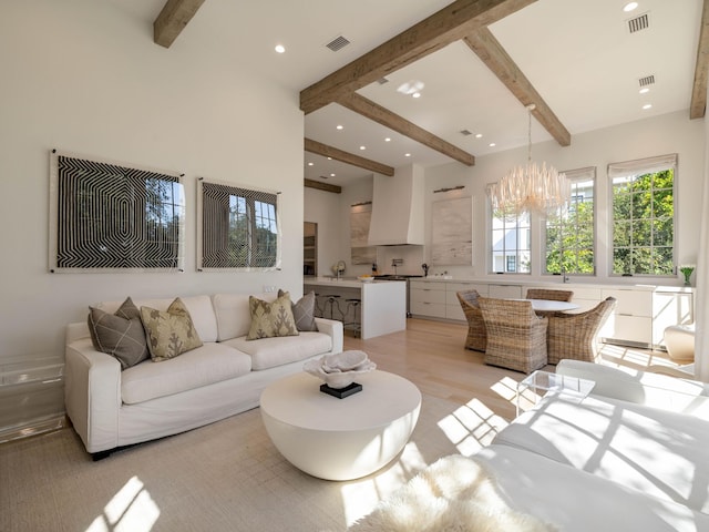 living room with sink, beamed ceiling, a chandelier, and light wood-type flooring