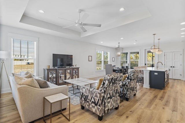 living room featuring a raised ceiling, ceiling fan, and light wood-type flooring