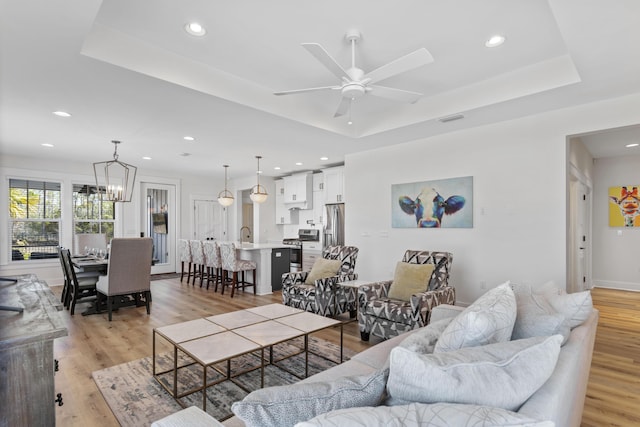 living room featuring a raised ceiling, ceiling fan with notable chandelier, and light wood-type flooring