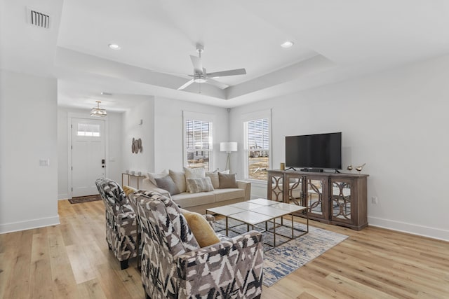 living room featuring a healthy amount of sunlight, a raised ceiling, and light wood-type flooring