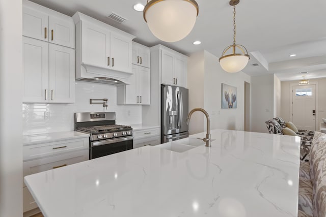 kitchen with white cabinetry, appliances with stainless steel finishes, light stone counters, and hanging light fixtures