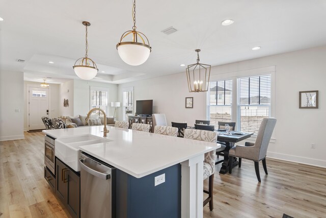 kitchen featuring sink, decorative light fixtures, stainless steel dishwasher, a kitchen island with sink, and light hardwood / wood-style floors