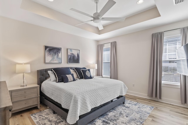 bedroom with a raised ceiling, ceiling fan, and light wood-type flooring