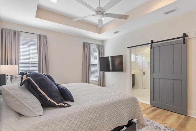 bedroom featuring a tray ceiling, a barn door, multiple windows, and light wood-type flooring