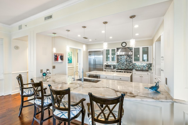 kitchen with sink, a breakfast bar, stainless steel appliances, decorative light fixtures, and wall chimney exhaust hood