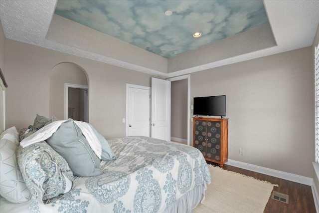 bedroom with a raised ceiling and dark wood-type flooring