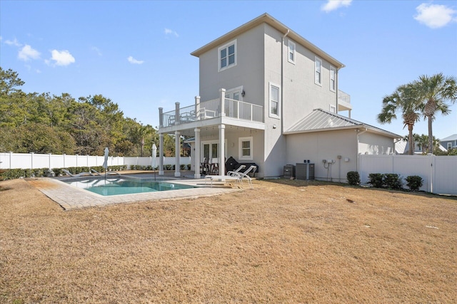 back of property featuring a patio, a balcony, a yard, central air condition unit, and a fenced in pool