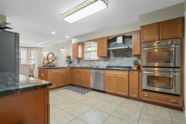 kitchen with appliances with stainless steel finishes, sink, backsplash, kitchen peninsula, and wall chimney exhaust hood