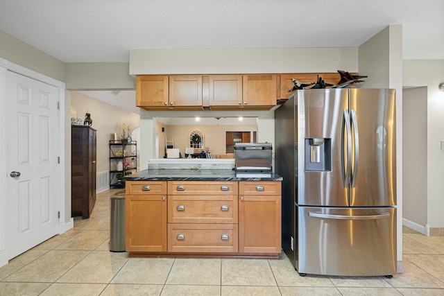 kitchen featuring light tile patterned floors, stainless steel fridge, a textured ceiling, and dark stone counters