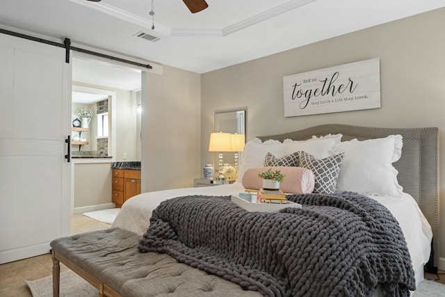 bedroom with light tile patterned floors, a tray ceiling, crown molding, a barn door, and ensuite bath