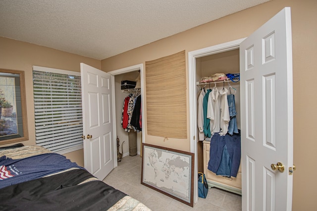 tiled bedroom with a walk in closet, a closet, and a textured ceiling