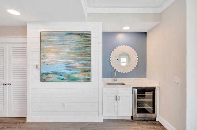 bar featuring sink, hardwood / wood-style flooring, wine cooler, light stone countertops, and white cabinets