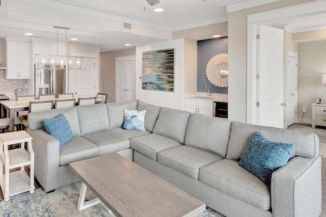 living room featuring wine cooler, ceiling fan with notable chandelier, ornamental molding, and indoor wet bar