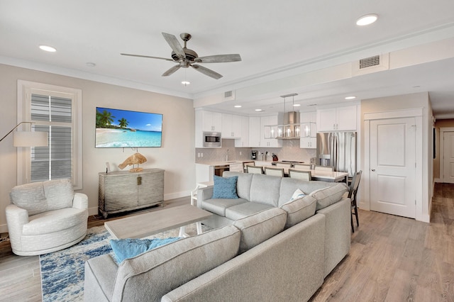 living room with light hardwood / wood-style flooring, ornamental molding, and ceiling fan