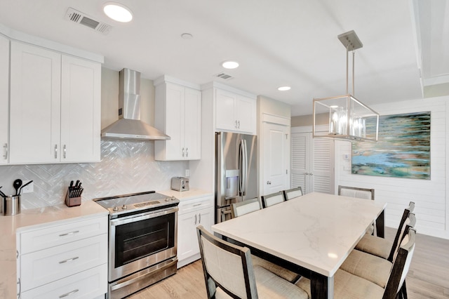 kitchen featuring white cabinetry, light hardwood / wood-style flooring, hanging light fixtures, stainless steel appliances, and wall chimney range hood