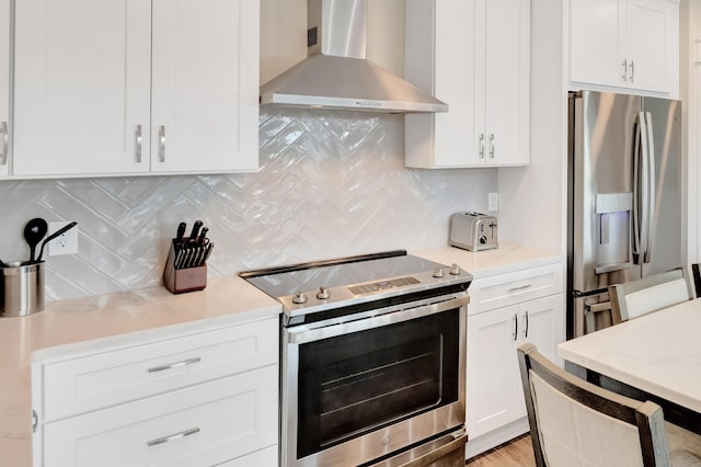 kitchen featuring wall chimney exhaust hood, white cabinetry, light stone counters, appliances with stainless steel finishes, and decorative backsplash