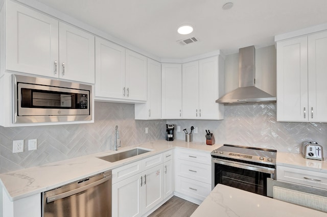 kitchen with wall chimney exhaust hood, sink, stainless steel appliances, light stone countertops, and white cabinets